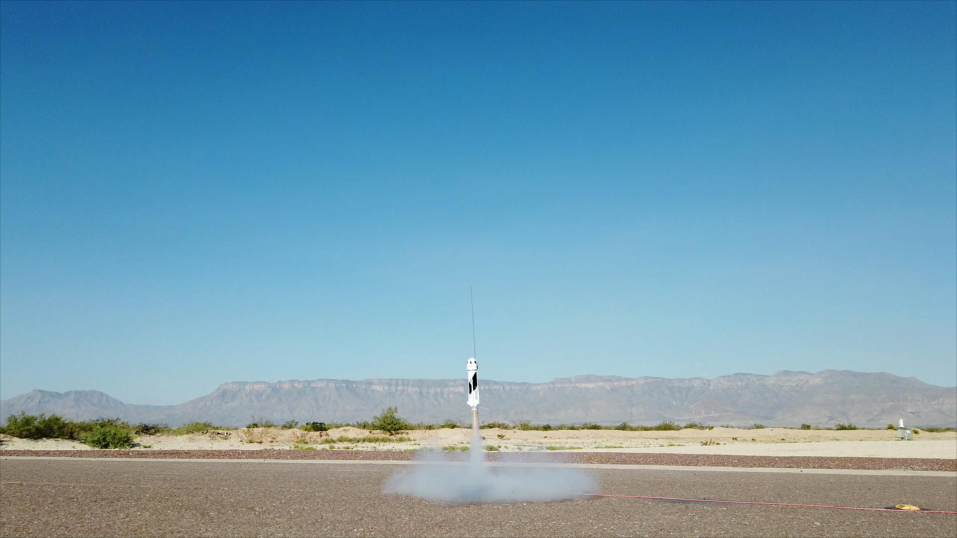 A small model rocket takes off from the ground in the Texas desert