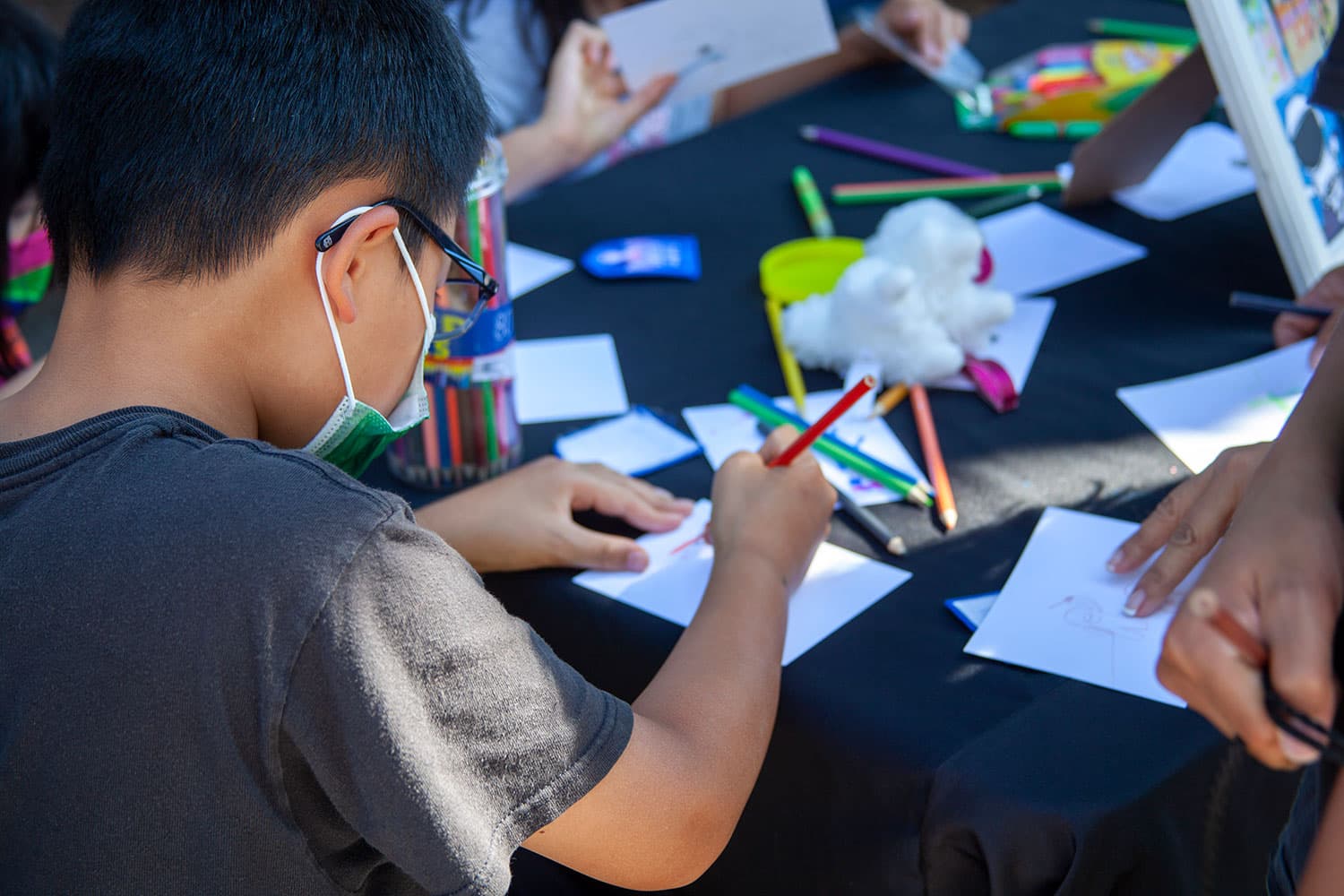 A child uses colored pencils to draw on a blank postcard