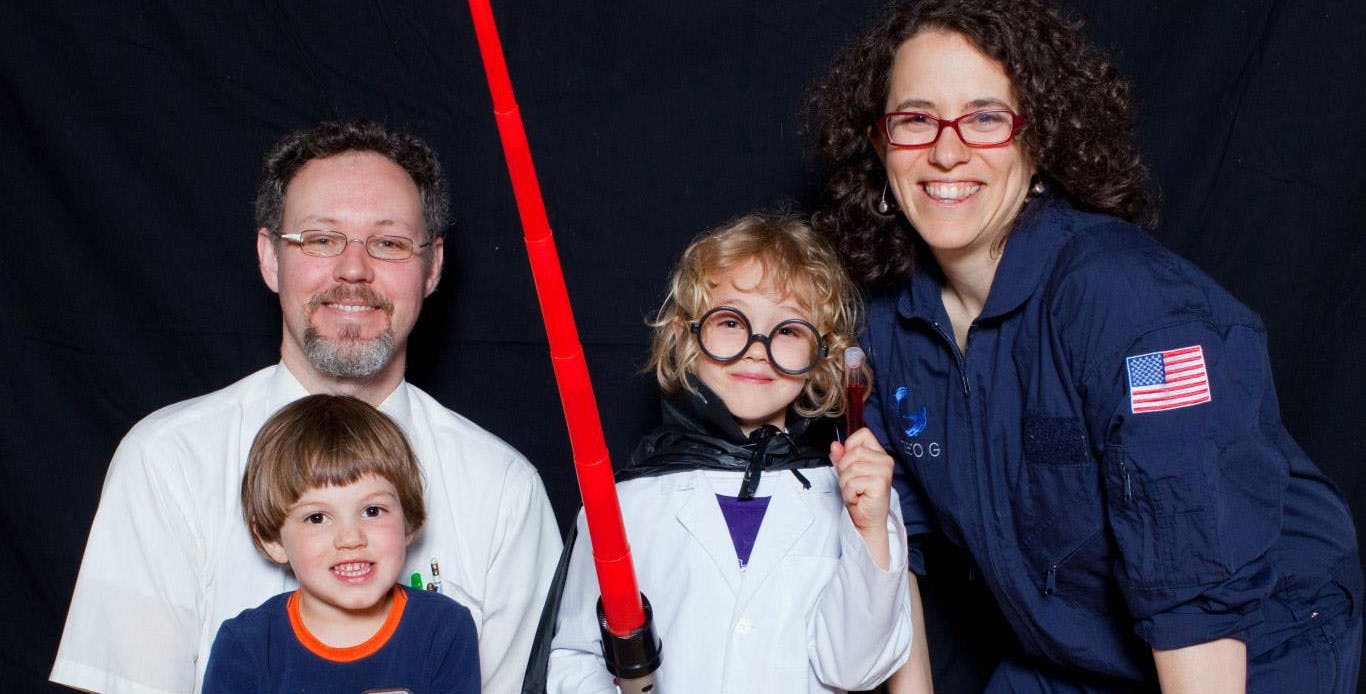 A family of 4 poses together; one child has a red lightsaber