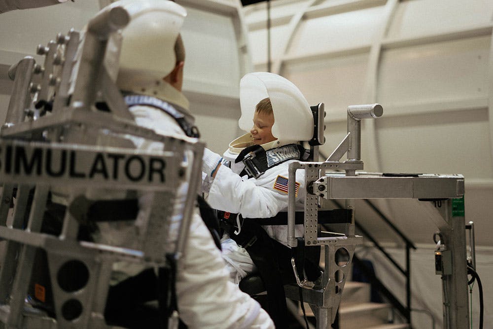 A child in a white spacesuit sits in a simulator