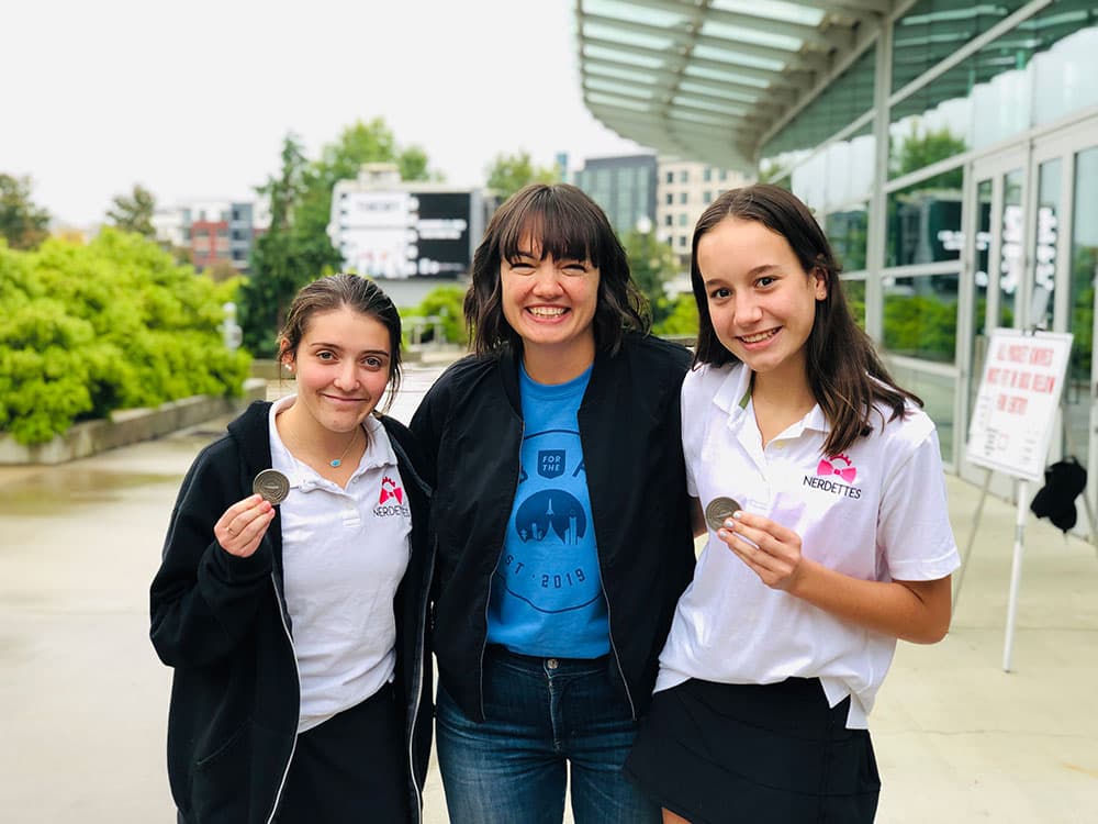 Sarah Knights, center, poses with two girls from the Nerdettes who are holding up Blue Origin coins